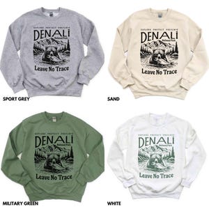 May include: Five crewneck sweatshirts in different colors: sport grey, sand, military green, white, and black. Each sweatshirt features a graphic print of a bear in a forest with the text "Explore Protect Preserve Denali National Park Leave No Trace".