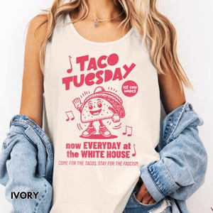 May include: Ivory tank top with a red graphic that reads "TACO TUESDAY" with a dancing taco illustration. The text "now EVERYDAY at the WHITE HOUSE" and "COME FOR THE TACOS, STAY FOR THE FASCISM" is also printed on the shirt.
