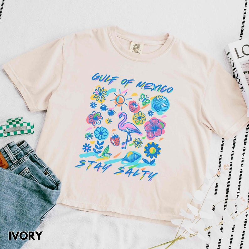 May include: Ivory t-shirt with a graphic print of a flamingo, flowers, and the text "Gulf of Mexico Stay Salty".