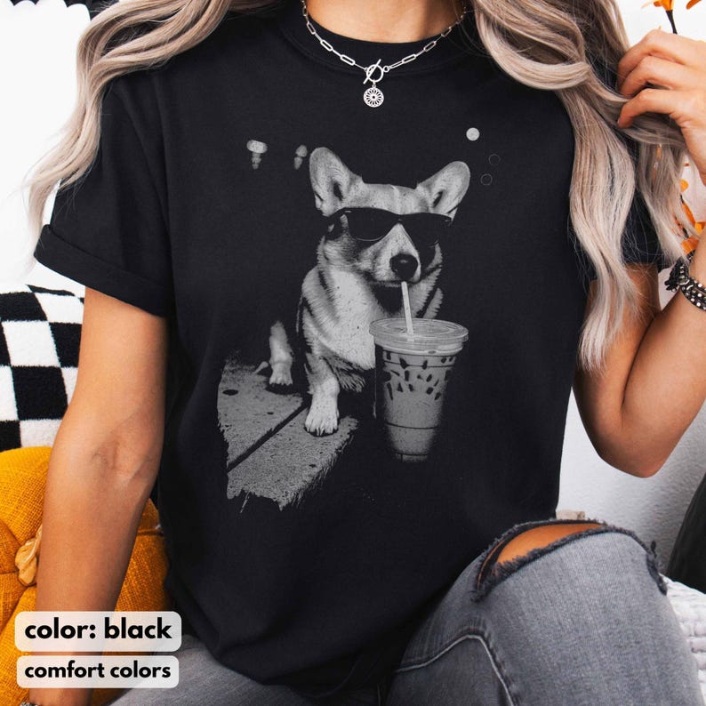 May include: Black t-shirt featuring a grayscale graphic of a corgi wearing sunglasses and drinking from a clear iced coffee cup with a straw. The text "color: black" and "comfort colors" is at the bottom of the shirt.