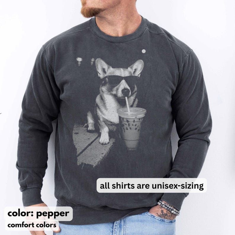 May include: Pepper-colored unisex sweatshirt featuring a graphic of a corgi wearing sunglasses and drinking an iced coffee. The text "all shirts are unisex-sizing" is displayed. The sweatshirt is from Comfort Colors.