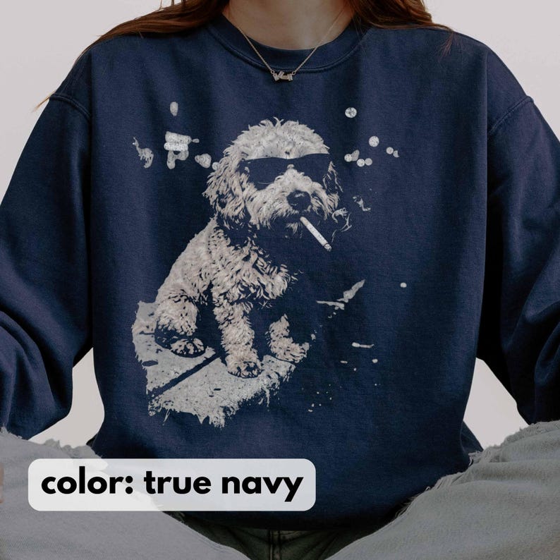 May include: True navy blue sweatshirt featuring a white graphic of a dog wearing sunglasses and smoking a cigarette. The dog is sitting on a white surface with white splatter details. The text "color: true navy" is at the bottom.