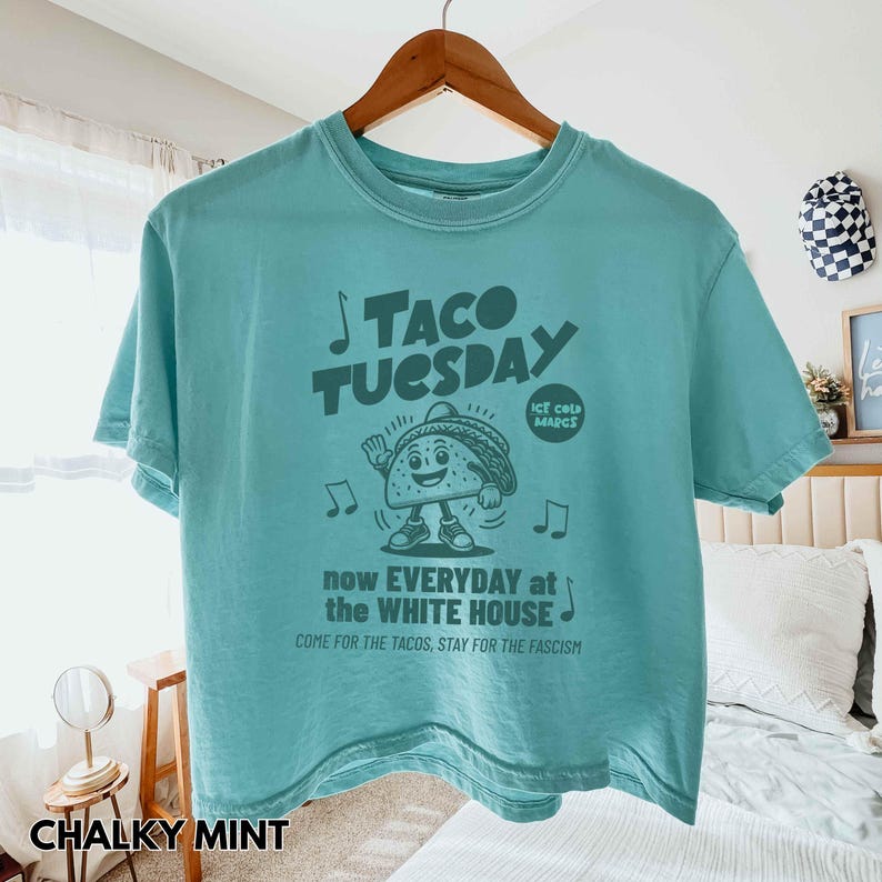 Pode incluir: Uma camiseta de cor menta giz com um gr&aacute;fico que diz "TACO TUESDAY" e um personagem de taco de desenho animado. A camisa tamb&eacute;m tem o texto "now EVERYDAY at the WHITE HOUSE".
