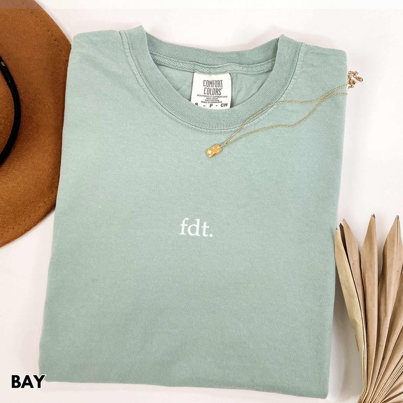 May include: A light green t-shirt with the text "fdt." embroidered on the front. The shirt is made of a soft, comfortable fabric and has a relaxed fit.