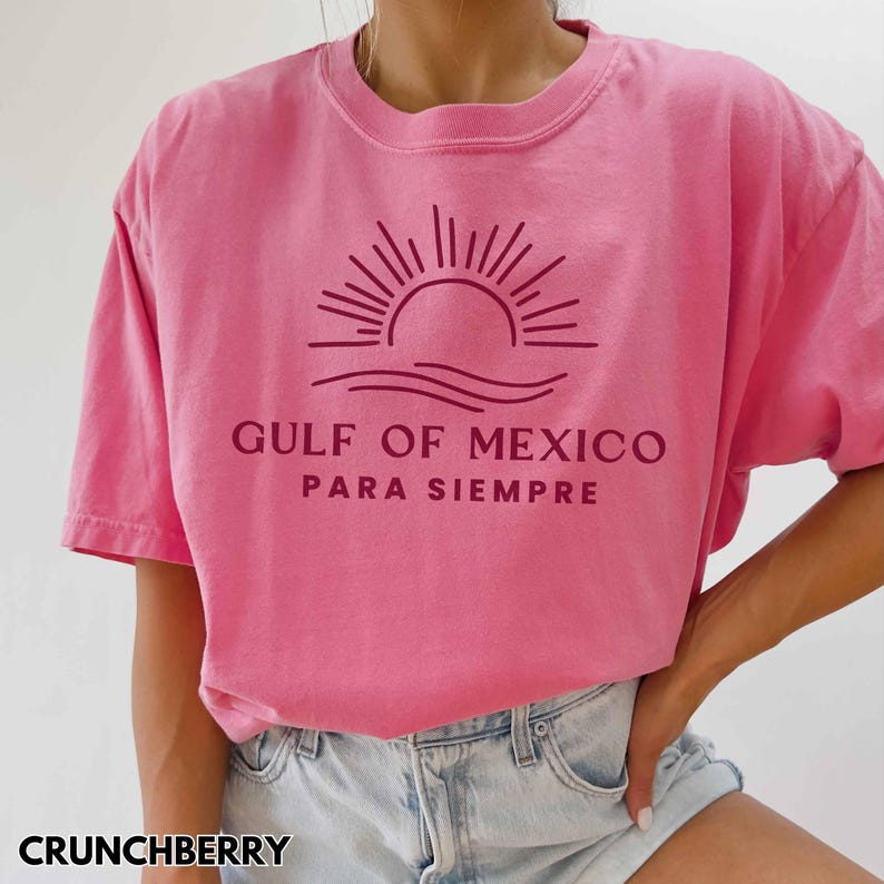 May include: Pink t-shirt with a maroon graphic of a sun setting over waves and the text "GULF OF MEXICO PARA SIEMPRE".