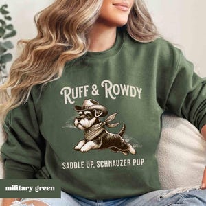 May include: A green sweatshirt with the text "Ruff & Rowdy" and a cartoon image of a miniature schnauzer wearing a cowboy hat and bandana. The text "Saddle Up, Schnauzer Pup" is below the image.