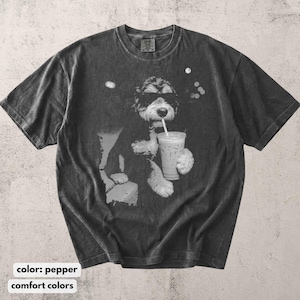K&ouml;nnte beinhalten: Pfefferfarbenes T-Shirt mit einer Schwarz-Wei&szlig;-Grafik eines Hundes mit Sonnenbrille, der aus einem transparenten Eiskaffeebecher mit Strohhalm trinkt. Das Shirt hat einen Rundhalsausschnitt und kurze &Auml;rmel. Der Text "comfort colors" steht unten.