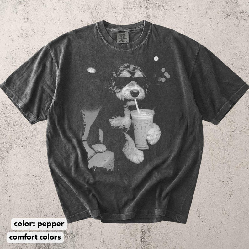 K&ouml;nnte beinhalten: Pfefferfarbenes T-Shirt mit einer Schwarz-Wei&szlig;-Grafik eines Hundes mit Sonnenbrille, der aus einem transparenten Eiskaffeebecher mit Strohhalm trinkt. Das Shirt hat einen Rundhalsausschnitt und kurze &Auml;rmel. Der Text "comfort colors" steht unten.