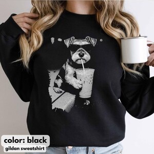 Pode incluir: Camisola Gildan preta com um gr&aacute;fico em tons de cinza de um c&atilde;o a usar &oacute;culos de sol e a beber de um copo transparente de caf&eacute; gelado. O texto "color: black" e "gildan sweatshirt" est&atilde;o na parte inferior.