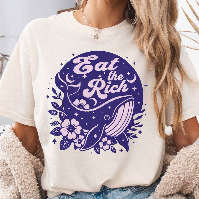 May include: A white t-shirt featuring a blue and pink whale graphic with the text "Eat the Rich" in a circle.