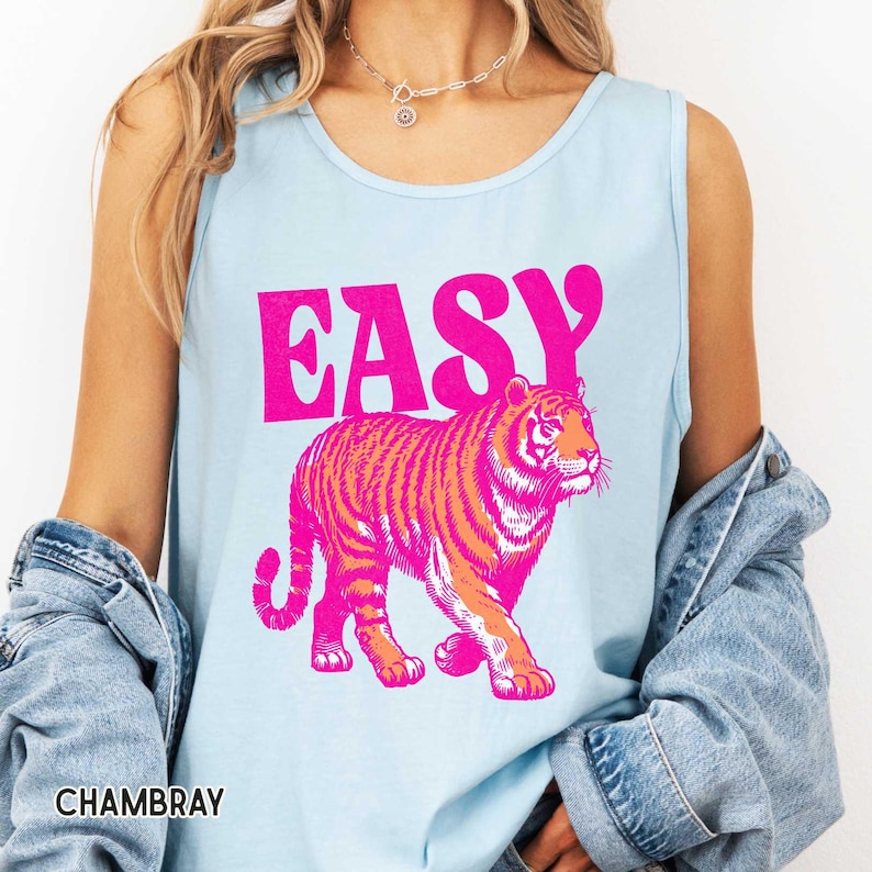 K&ouml;nnte beinhalten: Hellblaues Tanktop mit dem Wort "EASY" in leuchtend pinkfarbenen Blockbuchstaben &uuml;ber einer pink-orangenen Tigergrafik. Das Wort "CHAMBRAY" ist unten im Bild wei&szlig; gedruckt.