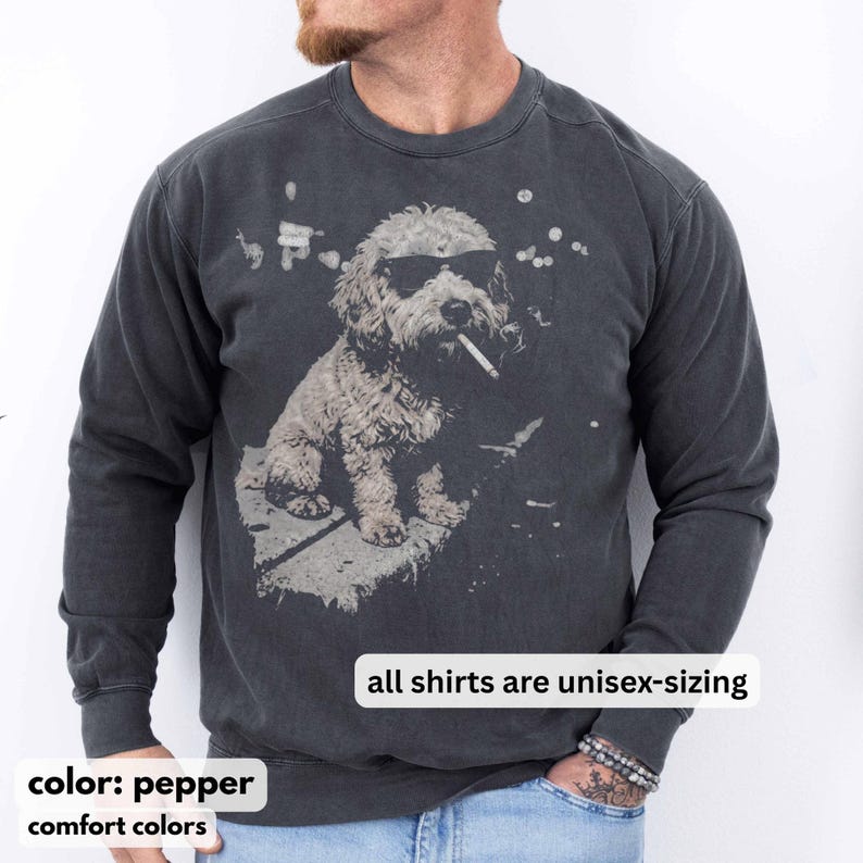 May include: Pepper-colored unisex sweatshirt featuring a graphic of a dog wearing sunglasses and smoking a cigarette. The dog is sitting on a stone surface. The text "all shirts are unisex-sizing" is displayed. The sweatshirt is part of the comfort colors collection.