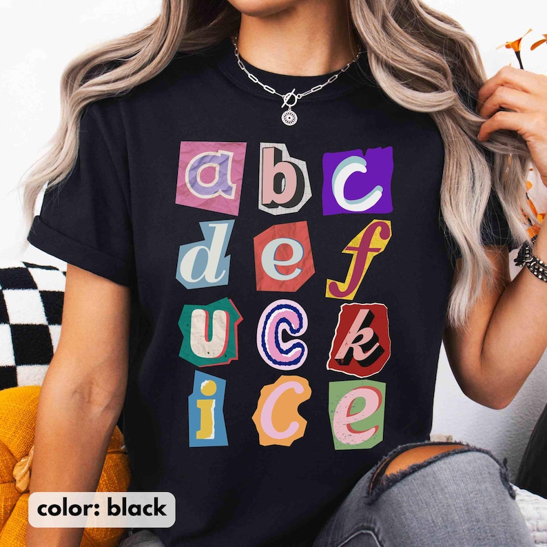 May include: Black t-shirt featuring a collage of colourful cut-out letters. The letters, in various fonts and colours, spell out the alphabet. The shirt also has the text "color: black" at the bottom.