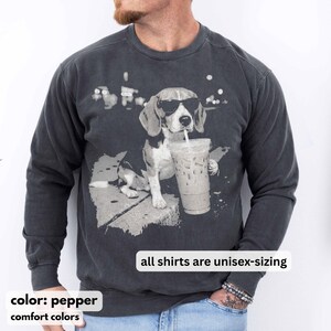 Puede incluir: Sudadera unisex color pimienta con un gr&aacute;fico de un beagle con gafas de sol bebiendo un caf&eacute; helado. Se muestra el texto "all shirts are unisex-sizing". La sudadera es de colores confort.