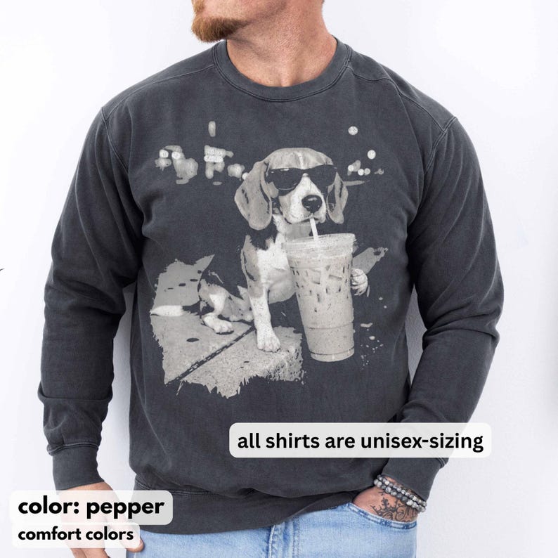 Puede incluir: Sudadera unisex color pimienta con un gr&aacute;fico de un beagle con gafas de sol bebiendo un caf&eacute; helado. Se muestra el texto "all shirts are unisex-sizing". La sudadera es de colores confort.