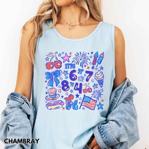Puede incluir: Camiseta sin mangas azul claro con un colorido dise&ntilde;o patri&oacute;tico. El dise&ntilde;o incluye fuegos artificiales, estrellas, cerezas, un helado y el n&uacute;mero 1776. La camiseta sin mangas est&aacute; hecha de un material suave, ideal para celebrar el D&iacute;a de la Independencia.