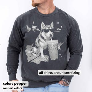 May include: Pepper-colored unisex sweatshirt featuring a graphic of a dog wearing sunglasses and drinking from a clear iced coffee cup. The text "all shirts are unisex-sizing" is displayed. The sweatshirt is from Comfort Colors.