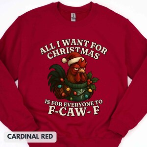 May include: Cardinal red sweatshirt with the text "ALL I WANT FOR CHRISTMAS IS FOR EVERYONE TO F-CAW-F." A rooster wearing a Santa hat and Christmas lights is in the center. The sweatshirt is a crew neck.