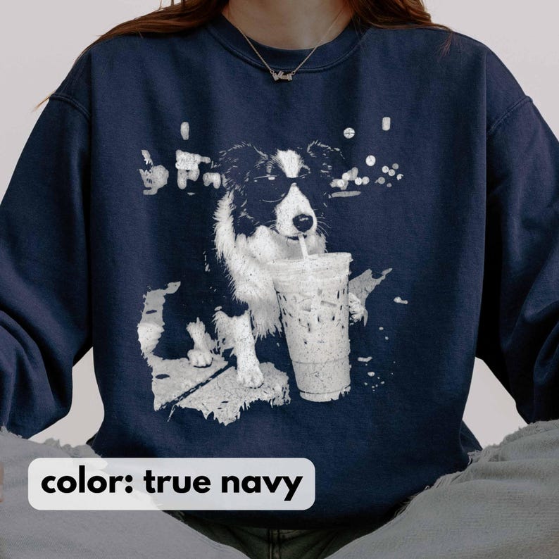 May include: True navy blue sweatshirt featuring a black and white graphic of a dog wearing sunglasses and drinking from a clear iced coffee cup with a straw. The text "color: true navy" is at the bottom of the image.
