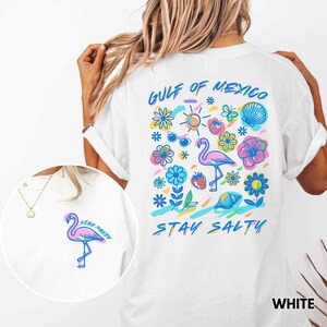 May include: White t-shirt with a colorful graphic design featuring a flamingo, flowers, a seashell, sunglasses, and the text "Gulf of Mexico" and "Stay Salty".