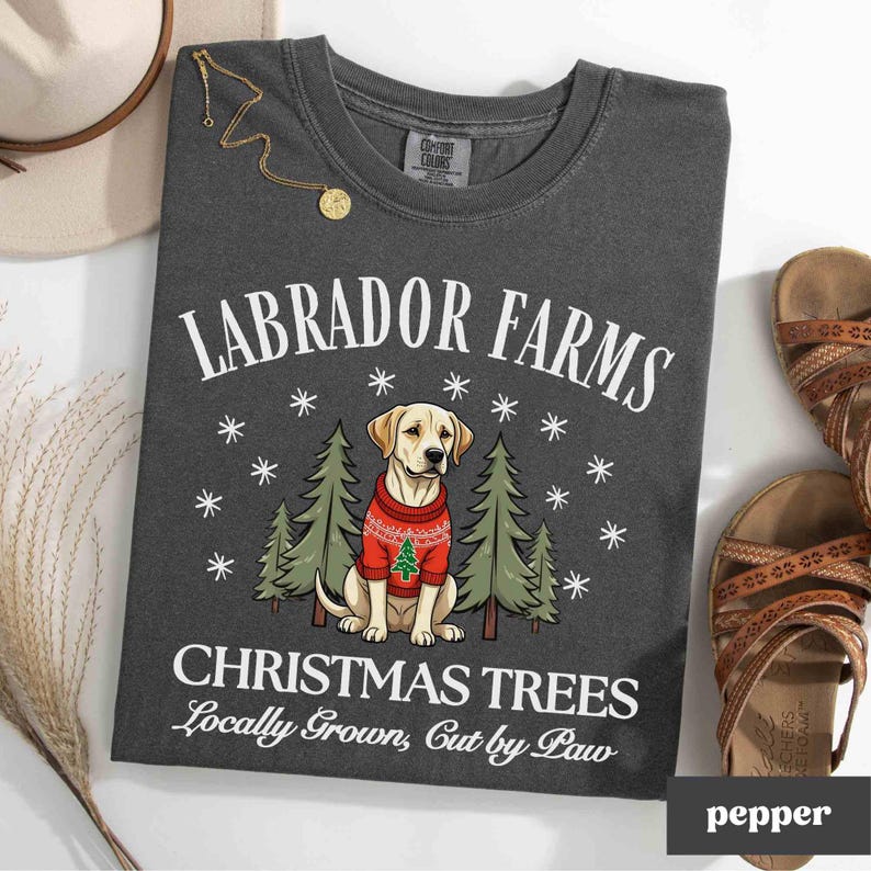 K&ouml;nnte beinhalten: Ein dunkelgraues T-Shirt mit dem Text "Labrador Farms Christmas Trees Locally Grown, Cut by Paw" und einem Cartoon-Bild eines gelben Labrador Retrievers, der einen roten Pullover mit einem kleinen Weihnachtsbaum tr&auml;gt.