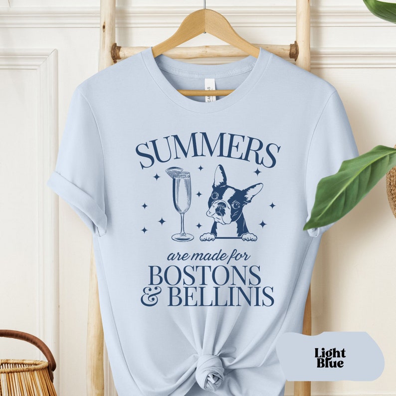 Puede incluir: Camiseta azul claro con un gr&aacute;fico de un Boston Terrier mirando por encima de un mostrador con una copa de Bellini. El texto de la camiseta dice "Summers are made for Bostons & Bellinis".