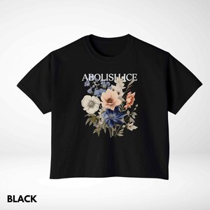 May include: Black t-shirt with a floral design and the text "ABOLISH ICE" in white. The floral arrangement includes white, pink, blue, and peach-colored flowers. The word "BLACK" is printed at the bottom of the shirt.