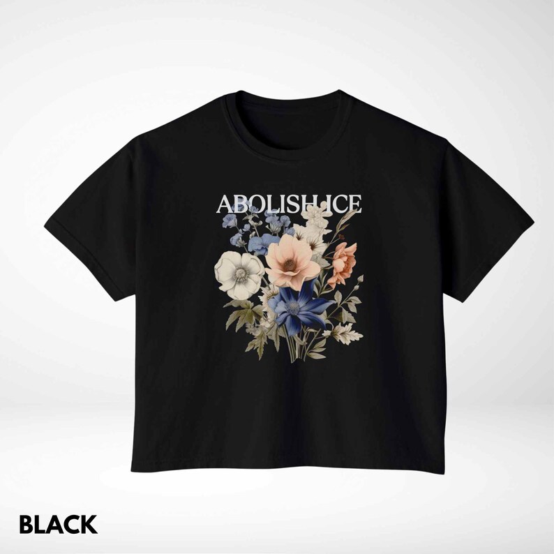 May include: Black t-shirt with a floral design and the text "ABOLISH ICE" in white. The floral arrangement includes white, pink, blue, and peach-colored flowers. The word "BLACK" is printed at the bottom of the shirt.