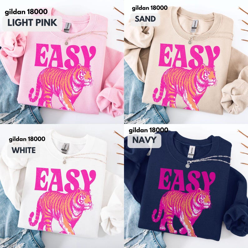 May include: Four Gildan 18000 crewneck sweatshirts in light pink, sand, white, and navy. Each sweatshirt features the word EASY in large pink letters above a graphic of a tiger in pink and orange tones. The garments have long sleeves and a crew neckline.