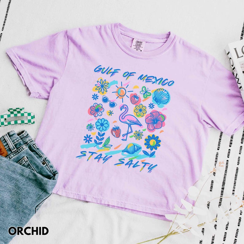 May include: A light purple t-shirt with a graphic print of a flamingo, flowers, and the text "Gulf of Mexico Stay Salty".