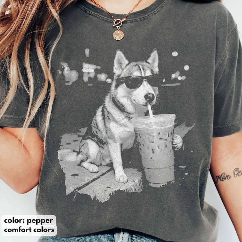 May include: Pepper-colored Comfort Colors t-shirt featuring a black and white graphic of a husky wearing sunglasses and drinking from a clear iced coffee cup. The text "color: pepper comfort colors" is at the bottom.