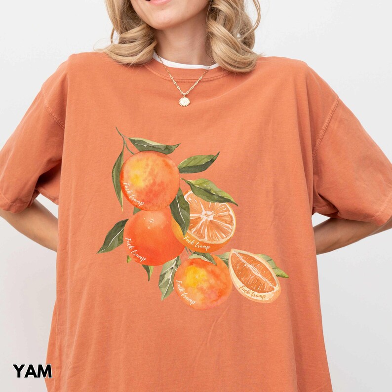 以下が含まれることがあります： オレンジ色のTシャツに、オレンジのグラフィックと、各オレンジに「Fruit Tramp」という文字が繰り返されて描かれています。