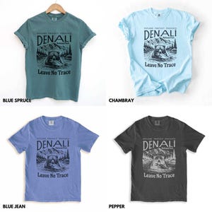 May include: Four t-shirts in different colors featuring a graphic of a bear in Denali National Park with the text "Explore Protect Preserve Denali National Park Leave No Trace". The colors are blue spruce, Chambray, blue jean, and pepper.