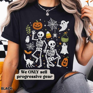 May include: Black Halloween-themed t-shirt with a festive design. The shirt features white skeletons, pumpkins, ghosts, spiders, and candy corn. The text "We ONLY sell progressive gear" is printed on the shirt.