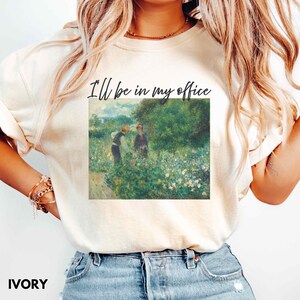 May include: Ivory t-shirt with the text "I'll be in my office" above a painting of two figures in a garden. The artwork is in a classic style, with a focus on nature and soft colours. The shirt is a casual, everyday wear item.