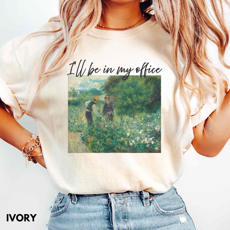 May include: Ivory t-shirt with the text "I'll be in my office" above a painting of two figures in a garden. The artwork is in a classic style, with a focus on nature and soft colours. The shirt is a casual, everyday wear item.