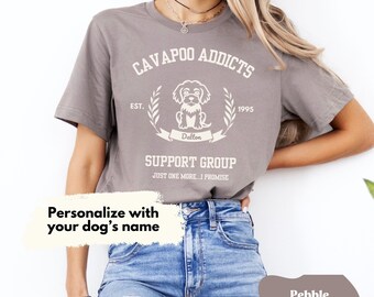 May include: Pebble brown t-shirt with the text "CAVAPOO ADDICTS SUPPORT GROUP" and a dog graphic. The shirt includes the text "EST. 1995" and "Dalton". The shirt also has the text "JUST ONE MORE...I PROMISE". The shirt is shown with the text "Personalize with your dog's name".