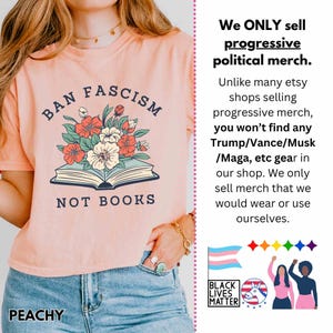 Op de afbeelding: Perzikkleurig T-shirt met de tekst "BAN FASCISM NOT BOOKS" boven een bloemenillustratie. Het shirt heeft ook het woord "PEACHY" aan de onderkant. Het shirt maakt deel uit van een progressieve politieke merch-collectie.