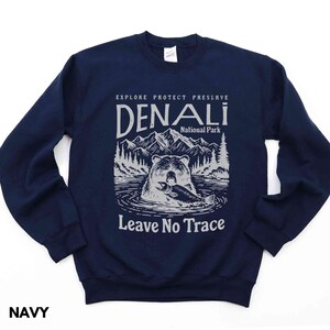 May include: Navy blue sweatshirt with a graphic of a bear fishing in a lake. The text "Explore Protect Preserve Denali National Park Leave No Trace" is printed on the sweatshirt.