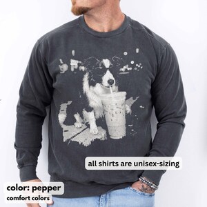 May include: Pepper-colored unisex sweatshirt featuring a black and white graphic of a dog drinking from a clear iced coffee cup. The text "all shirts are unisex-sizing" is displayed. The sweatshirt is part of the comfort colors collection.