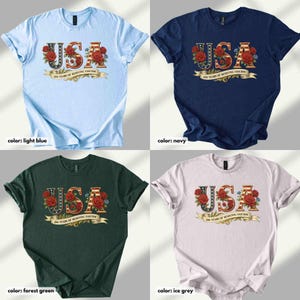 Op de afbeelding: Vier t-shirts in lichtblauw, marineblauw, bosgroen en ijsgrijs. Elk shirt toont het woord "USA" in een decoratief lettertype met rode rozen en een banner met de tekst "200 YEARS OF RESISTING FASCISM".