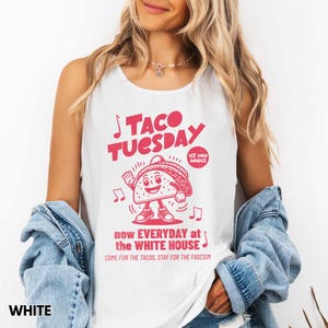 May include: White tank top with a pink graphic that reads "TACO TUESDAY" with a cartoon taco character. The text "now EVERYDAY at the WHITE HOUSE" and "COME FOR THE TACOS, STAY FOR THE FASCISM" is also printed on the shirt.