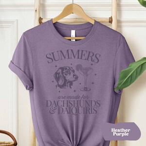 May include: A purple t-shirt with the text "SUMMERS are made for  DACHSHUNDS & DAIQUIRIS" and a graphic of a dachshund and a cocktail glass.