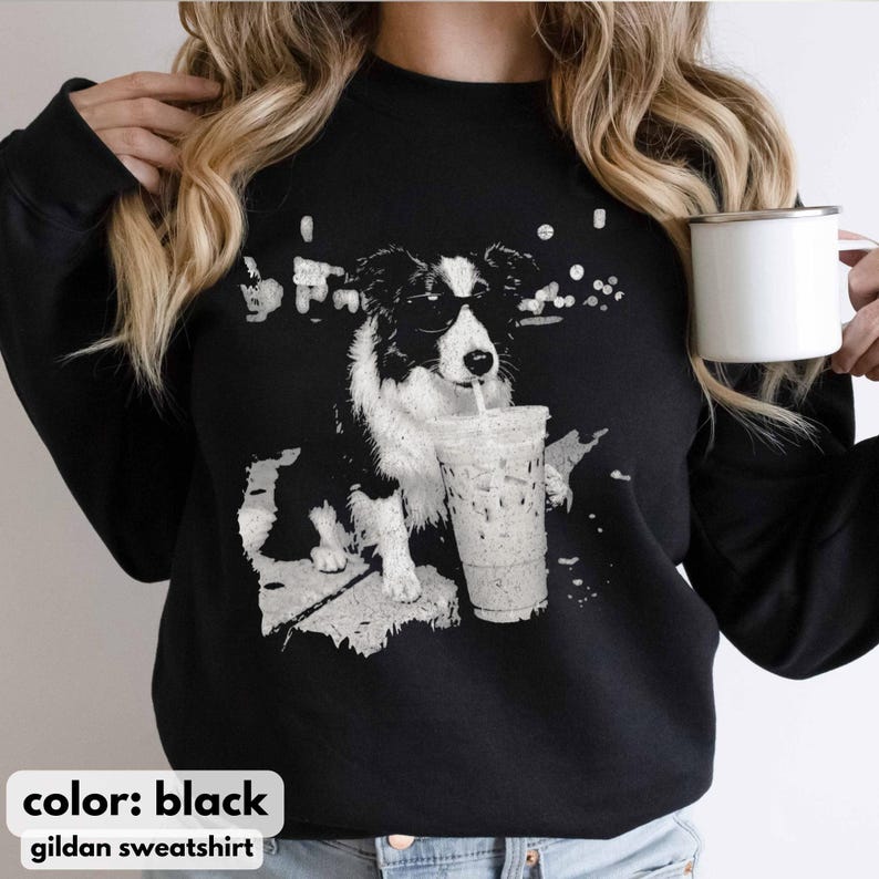 May include: Black sweatshirt featuring a graphic of a black and white dog wearing sunglasses and drinking from a clear iced coffee cup. The text "color: black" and "gildan sweatshirt" are at the bottom.
