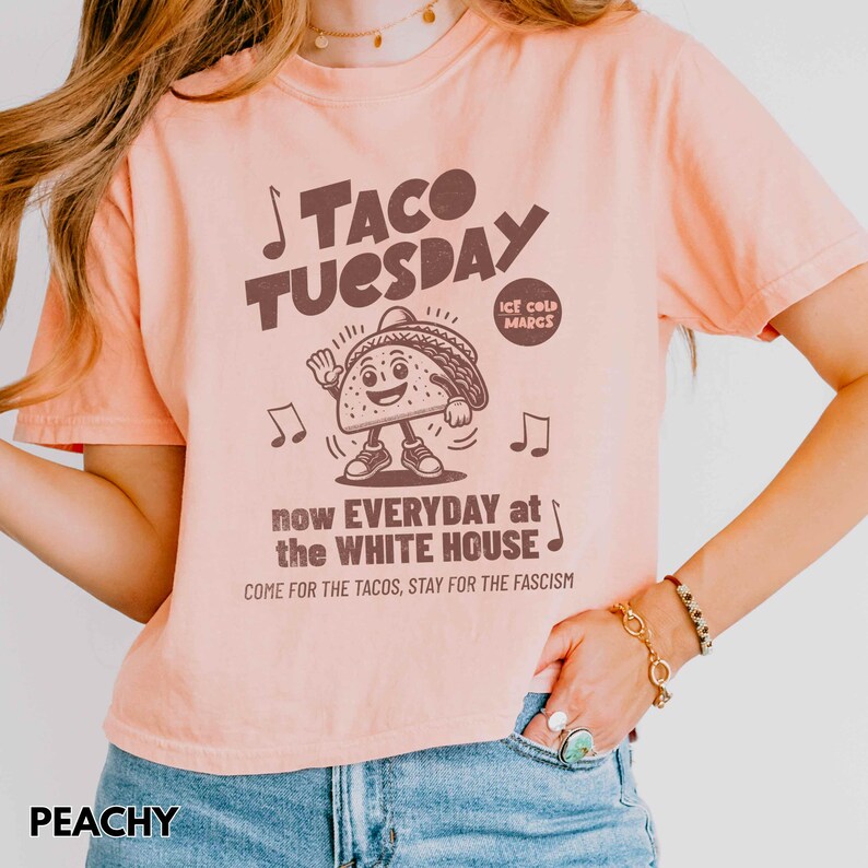 Pode incluir: Uma camiseta cor de p&ecirc;ssego com o texto "TACO TUESDAY" e um personagem de desenho animado de taco. A camisa tamb&eacute;m apresenta o texto "now EVERYDAY at the WHITE HOUSE" e "COME FOR THE TACOS, STAY FOR THE FASCISM".