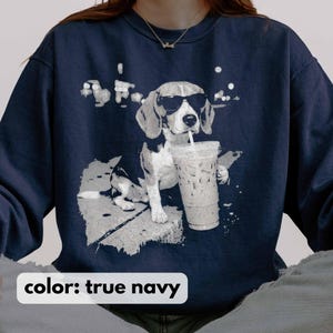 Puede incluir: Sudadera azul marino con un gr&aacute;fico de un beagle con gafas de sol y sosteniendo un caf&eacute; helado. El perro est&aacute; representado en una pose relajada, con una pajita en la boca. El texto "color: true navy" est&aacute; en la parte inferior.