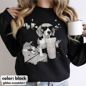Puede incluir: Sudadera negra con un gr&aacute;fico en escala de grises de un beagle con gafas de sol bebiendo caf&eacute; helado. El dise&ntilde;o incluye el texto "color: black" y "gildan sweatshirt" en la parte inferior. El perro es el foco central.