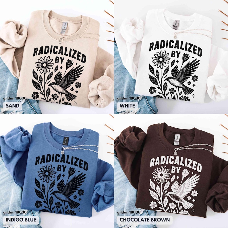 May include: Four Gildan 18000 sweatshirts in sand, white, indigo blue, and chocolate brown. Each sweatshirt features the text "RADICALIZED BY" above a floral and bird graphic in black. A silver necklace is draped on each shirt.