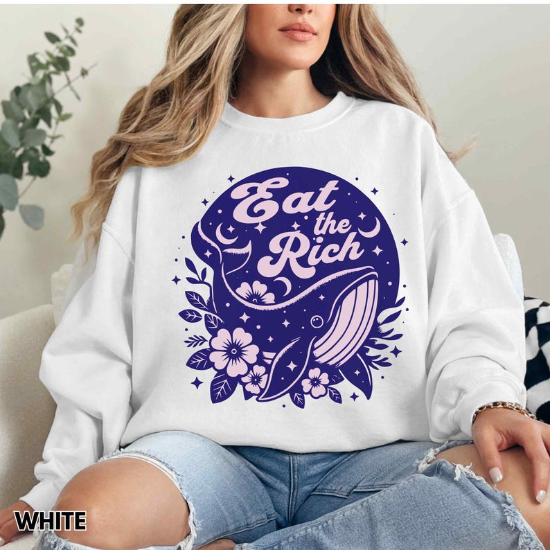 May include: White sweatshirt featuring a blue whale graphic and the text "Eat the Rich" in pink lettering. The whale is surrounded by pink flowers and stars.