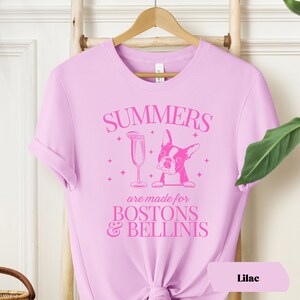 Puede incluir: Camiseta lila con un dise&ntilde;o gr&aacute;fico rosa que muestra un Boston Terrier asom&aacute;ndose por encima de una copa de Bellini con el texto "Summers are made for Bostons & Bellinis".